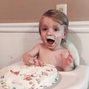 William smiling while enjoying a cake in his high chair