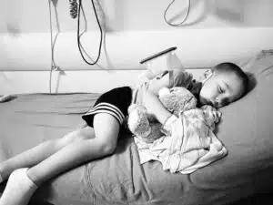 Beckett - sleeping in hospital bed with ice pack on back, snuggling bear and blanket