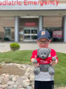 Beckett - holding Cardinal Glennon bear smiling in front of the hospital emergency department entrance