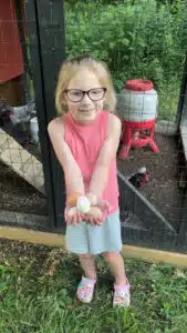 Kenzie - posing, holding chicken eggs in front of coop