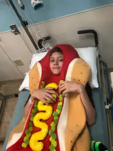 Logan - laying in hospital bed wearing a hotdog costume