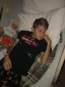Logan - sleeping in hospital bed with "Hope" bear next to him