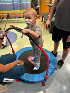 Easton - in therapy on small trampoline wearing a medical mask