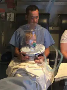Colten wearing a helmet ventilator and held by dad, Justen