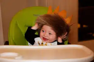 Colten smiling in a high chair wearing lion and crown head covering