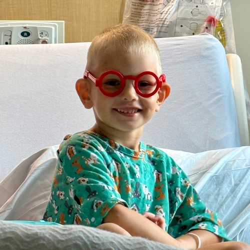 Wyatt smiling in his hospital bed wearing large red glasses