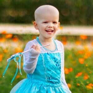 Cardinal Glennon patient Bristol holding a wand while wearing an Elsa dress in a field of flowers