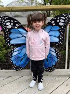 Cardinal Glennon patient Bristol posing in front of large butterfly wings at the Butterfly House