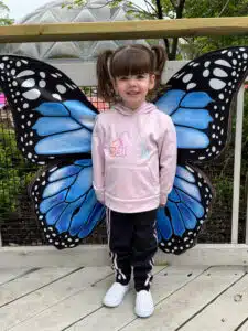 Cardinal Glennon patient Bristol posing in front of large butterfly wings at the Butterfly House