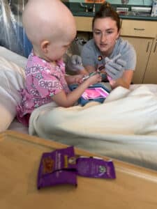 Cardinal Glennon patient Bristol sitting in a hospital bed receiving treatment from her oncology nurse