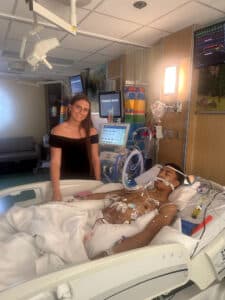 Quincy's girlfriend in prom dress bedside in the PICU while Quincy recovers
