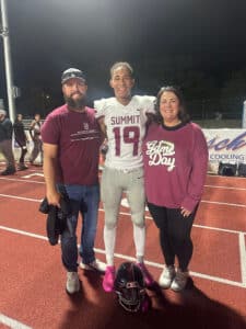 Quincy posing with his parents after a football game on the field