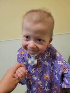 photo of a little girl with a trach in a hospital gown smiling