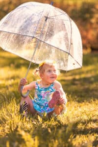 professional portrait of a little girl outside in the sunshine holding a clear umbrella and smiling