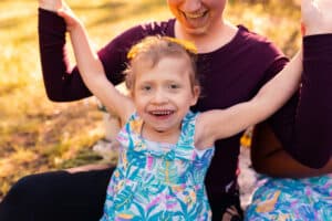 photo of a little girl outside smiling with her mother behind holding up her arms