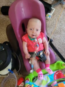 photo of a little girl in an accessible seat with a trach in front of a play table