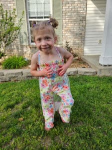 photo of a little girl standing by herself in a yard smiling