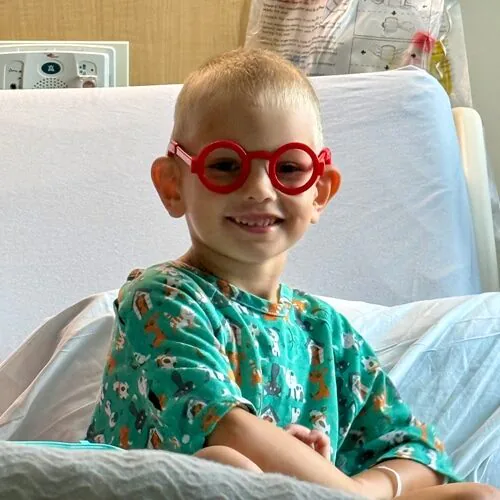 Wyatt smiling in his hospital bed wearing large red glasses